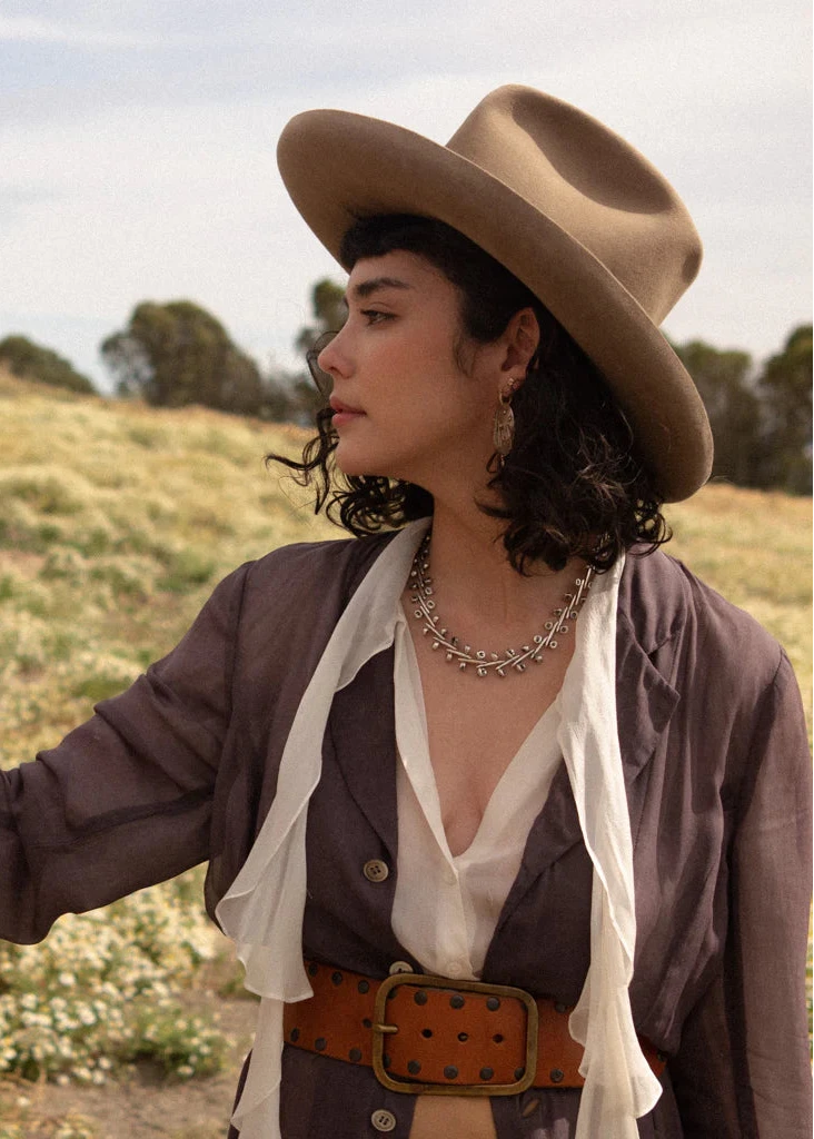 Woman wearing the Ocotillo Collar Necklace with a wide-brimmed hat, showing how the sculptural silver chain complements a layered outfit.
