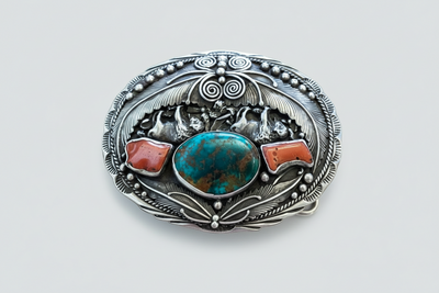 Ornate silver-tone Western belt buckle featuring a central blue-green stone, reddish accents, and intricate engraved metalwork.
