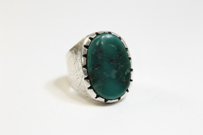 Silver-tone ring featuring a large oval green gemstone with dark natural-looking markings, photographed against a white background.