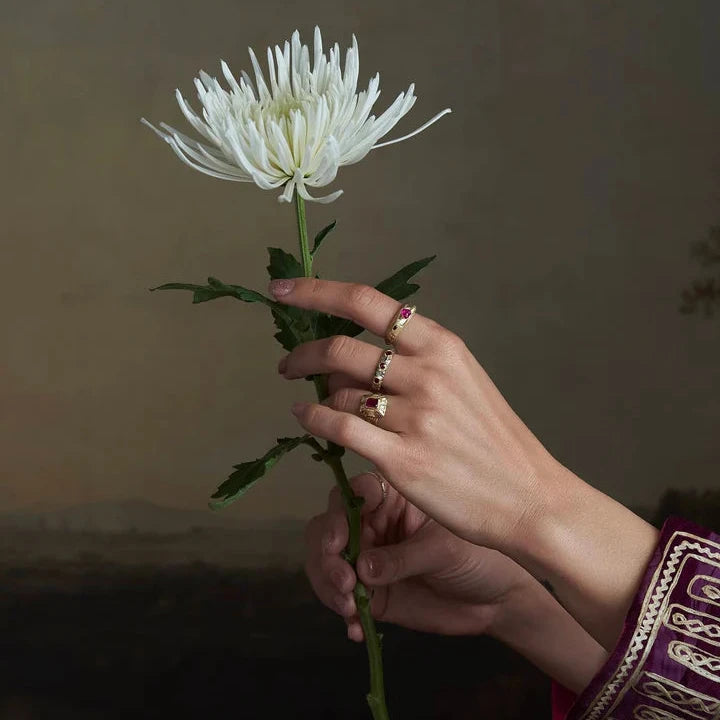 Pebbly Ring in 14k yellow and white gold worn on a model's hand holding a white flower, highlighting its sculptural design and ruby accents.