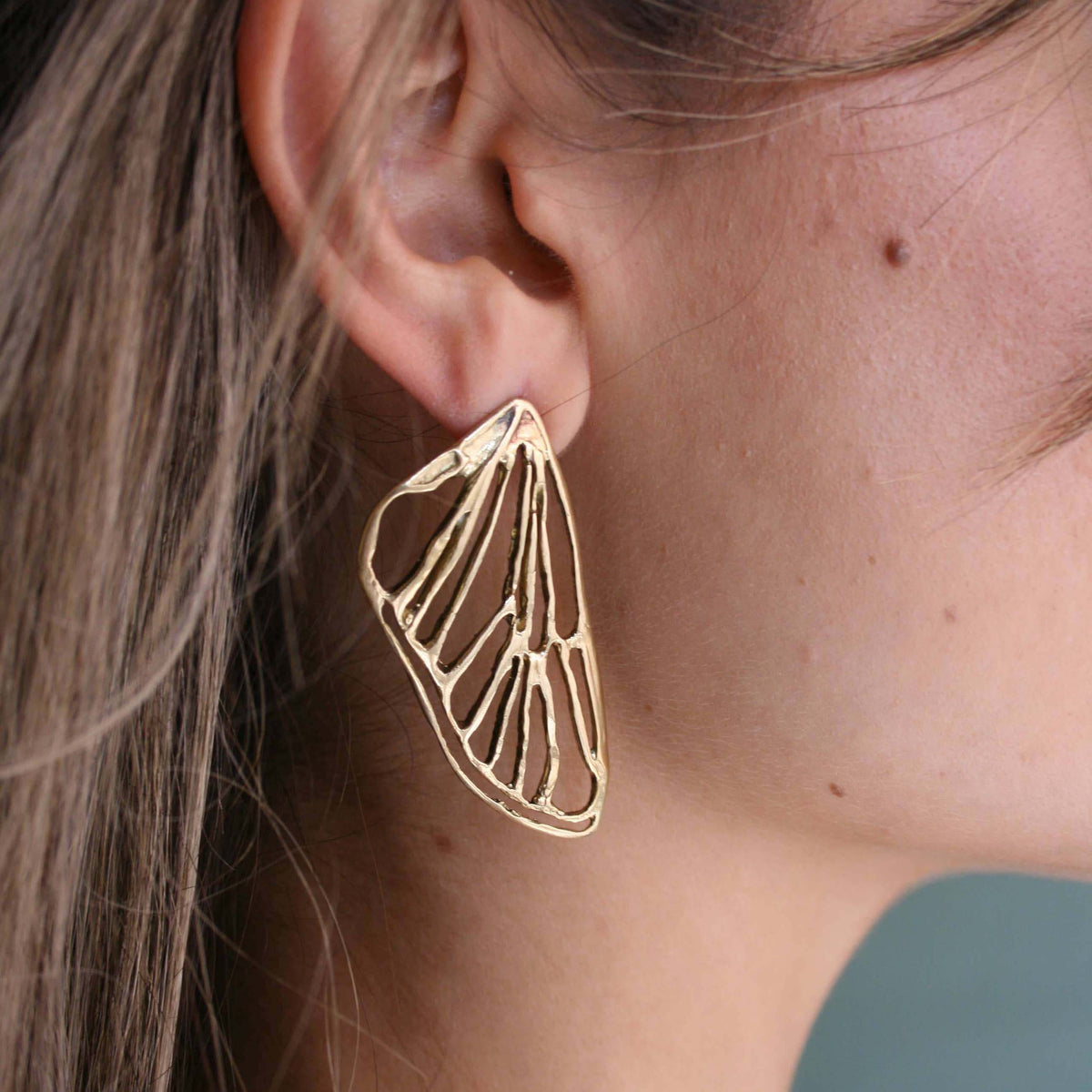 Close-up of a model wearing a petite gold-plated cicada wing earring, showing its lightweight openwork design and delicate 1.5-inch length.