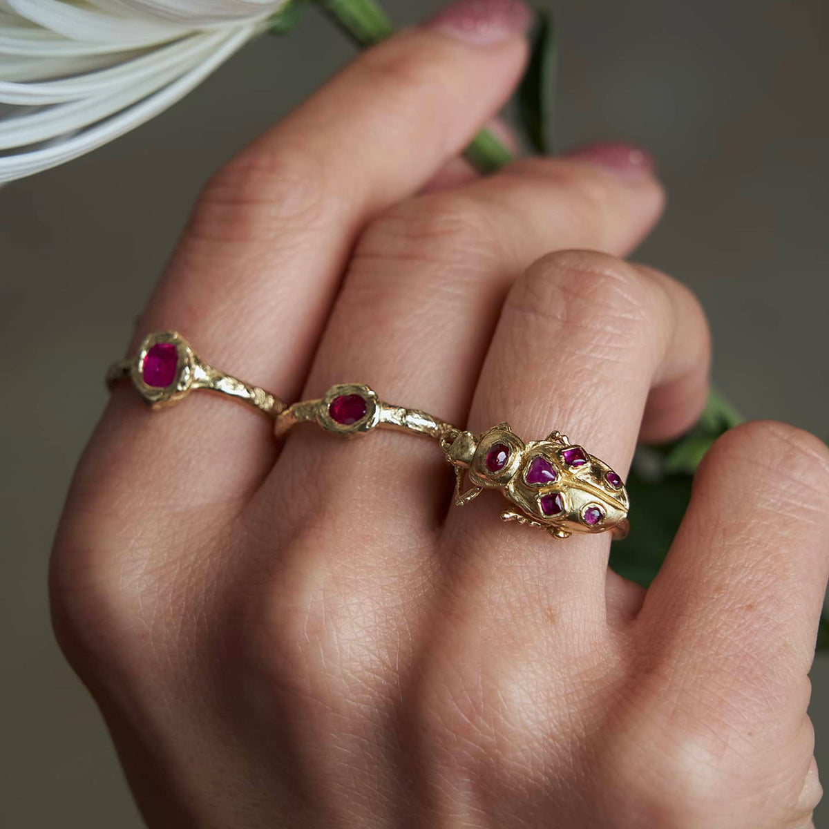 Close-up of the Petite Ruby Petra Ring worn on a hand alongside other gold rings, featuring its natural ruby and organic textured band.