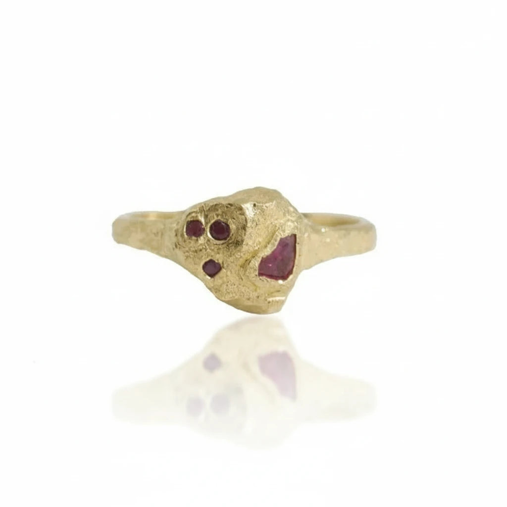 Front view of the Petra Ruby Ring by Alexis Pavlantos, showcasing its sculptural hollow rock setting, four natural rubies, and organic 14k yellow gold texture.