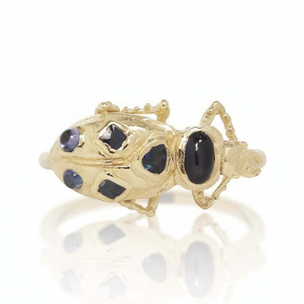 Front angled view of the Pinacate Beetle Ring in recycled 14k yellow gold, featuring a sculptural beetle design with dark cabochon sapphires.