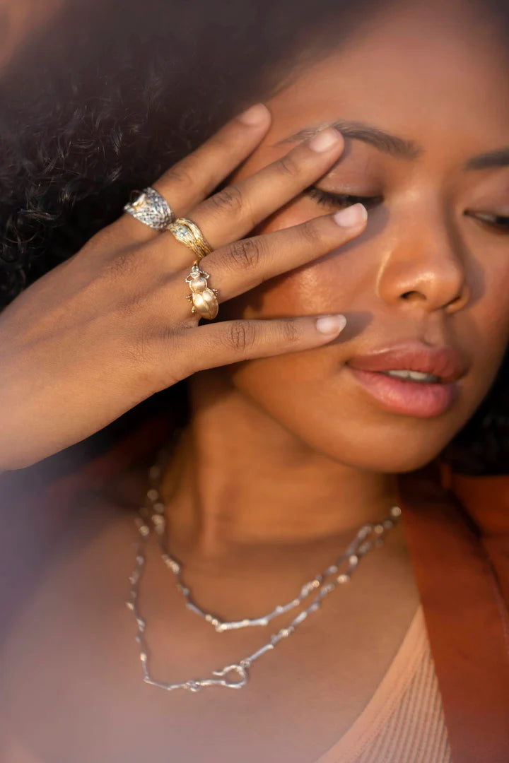 Model wearing the 14k yellow gold Pinacate Beetle Ring alongside other gold jewelry, showcasing its sculptural insect design and scale on the hand.