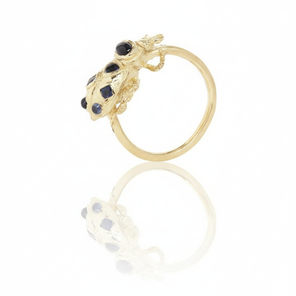 Side view of the handcrafted 14k yellow gold Pinacate Beetle Ring, showing its raised beetle sculpture, gemstone settings, and open band.
