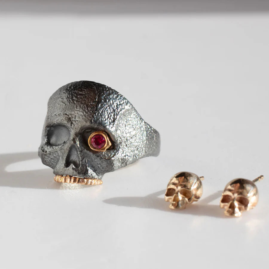 Detailed side view of The Masque of the Red Death Skull Ring featuring textured sterling silver, a red ruby eye, and yellow gold details.