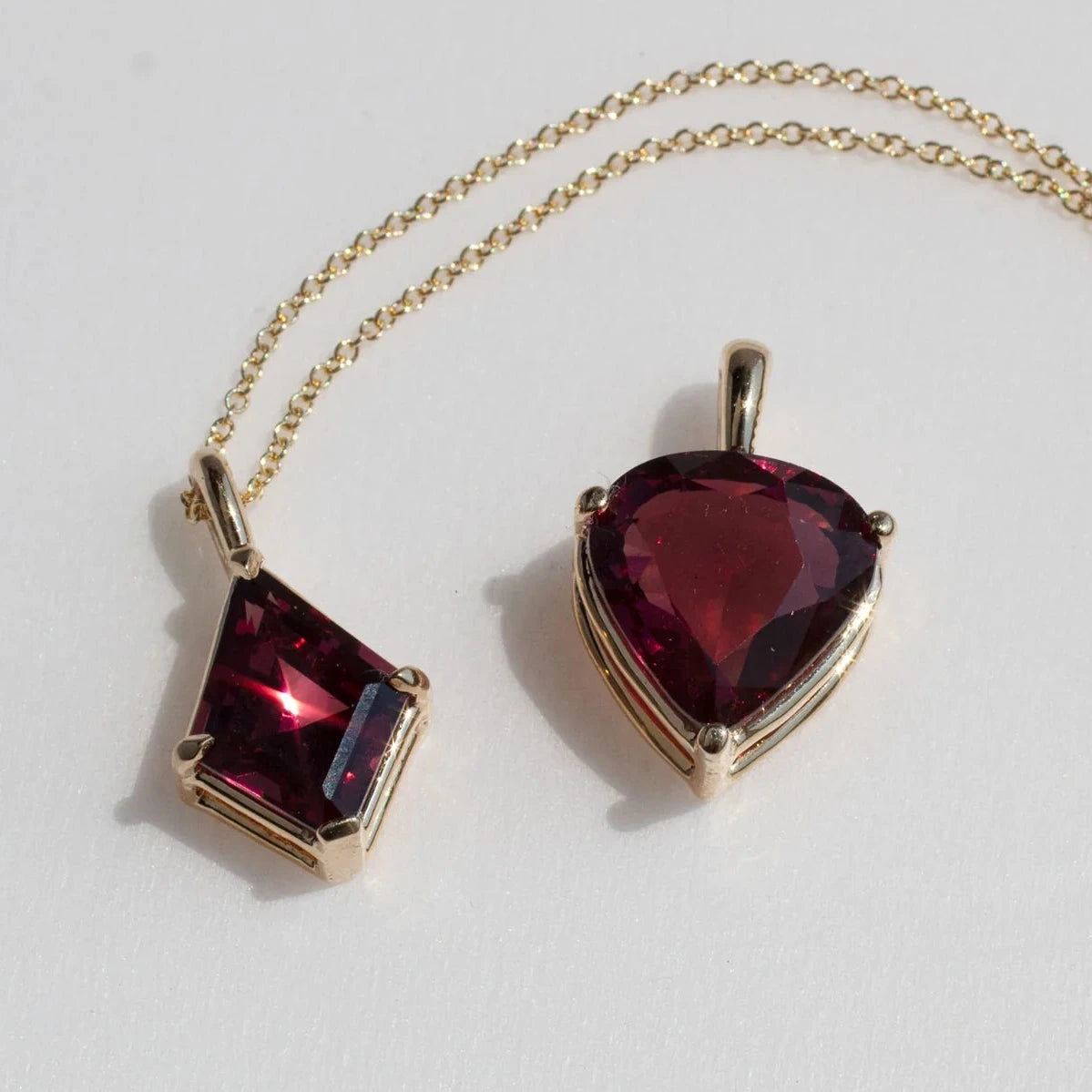 Michaela Farkasovska's kite-shaped rhodolite garnet pendant displayed with a gold chain, highlighting its faceted gemstone and delicate gold setting.