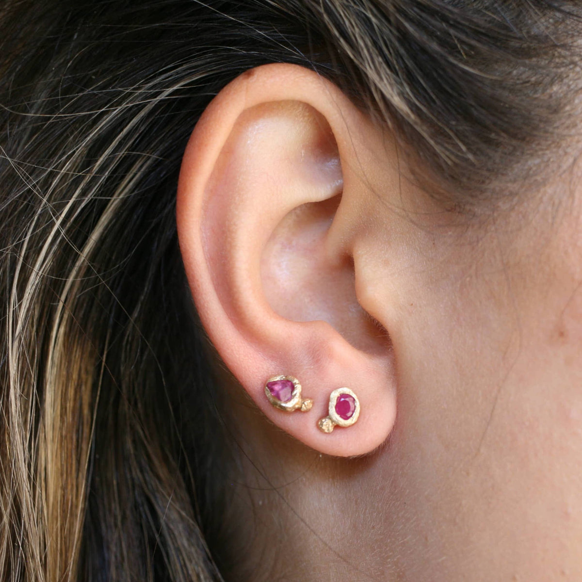 Model wearing Ruby Petra Stud Earrings in 14k yellow gold alongside other petite gemstone studs, showcasing their natural ruby color and everyday styling.