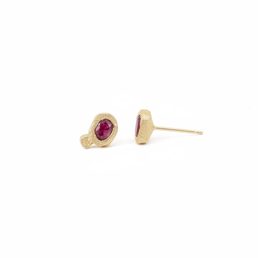 Angled view of Ruby Petra Stud Earrings in 14k yellow gold, featuring natural red rubies set in hand-carved, rock-textured gold settings with delicate posts.