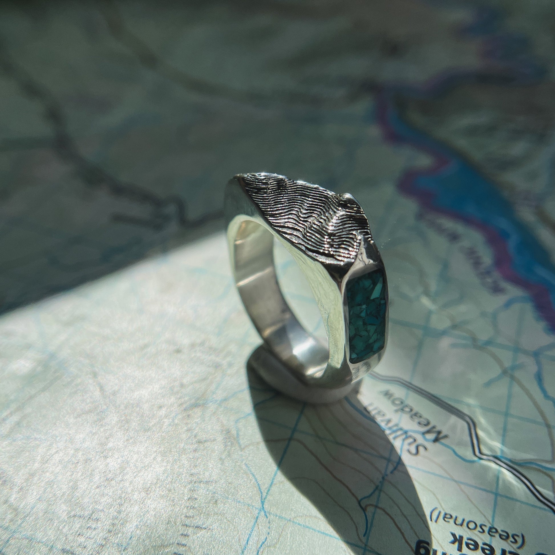 Sterling silver Sandia Crest topo ring with crushed turquoise photographed outdoors on stone.