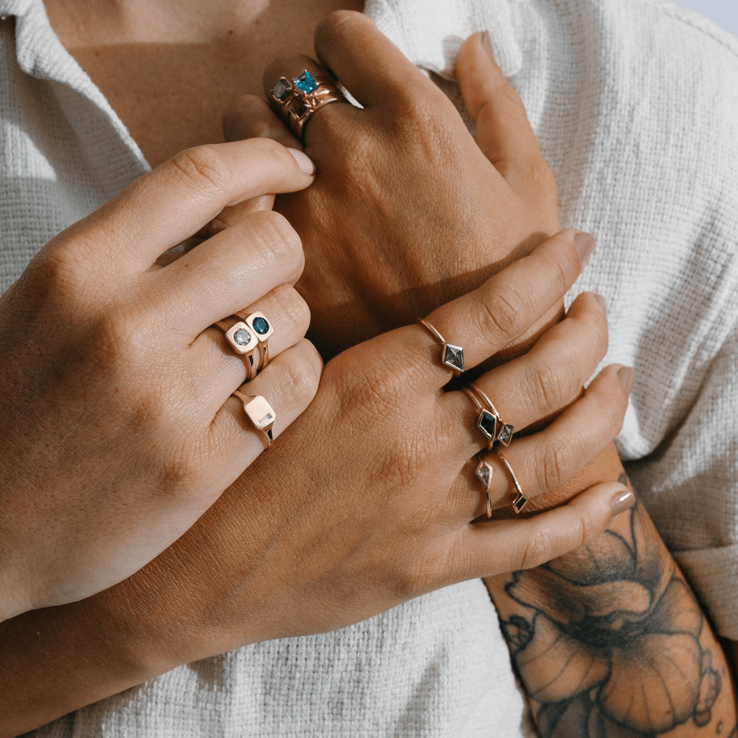 Multiple hands wearing layered gold rings, including the Sapphire Kite Ring, in soft natural light.