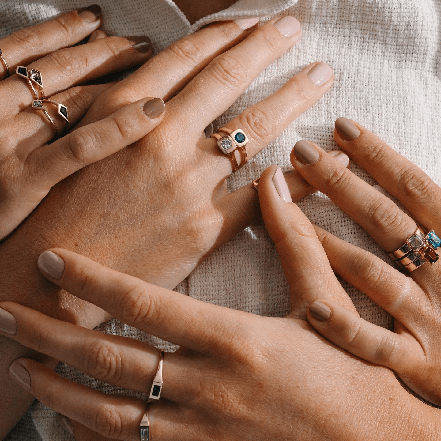 Hands stacked with various gold rings, including the Sapphire Kite Ring, photographed in bright natural light.