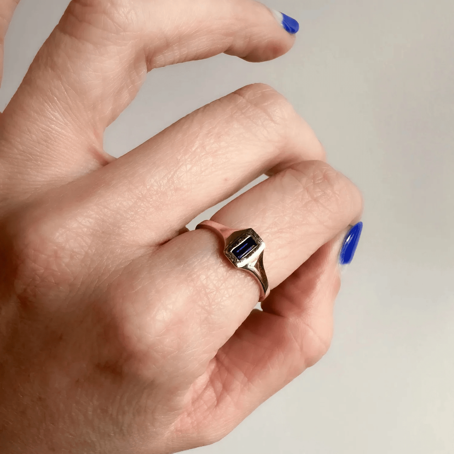 14k yellow gold Sapphire Passage Ring with a blue baguette sapphire worn on a hand in natural light.