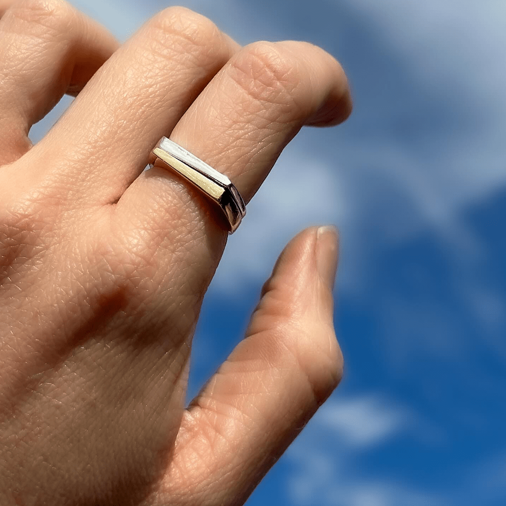 Sterling silver tapered ring worn on a hand against a bright blue sky.