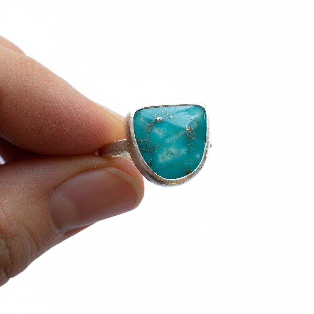 Turquoise ring held between fingers on a white background