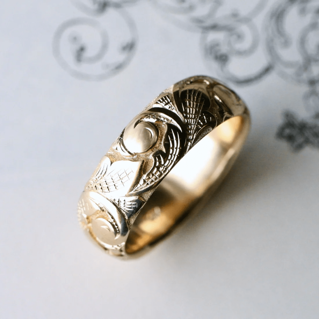 Slim 14k gold acanthus engraved band photographed at an angled view.