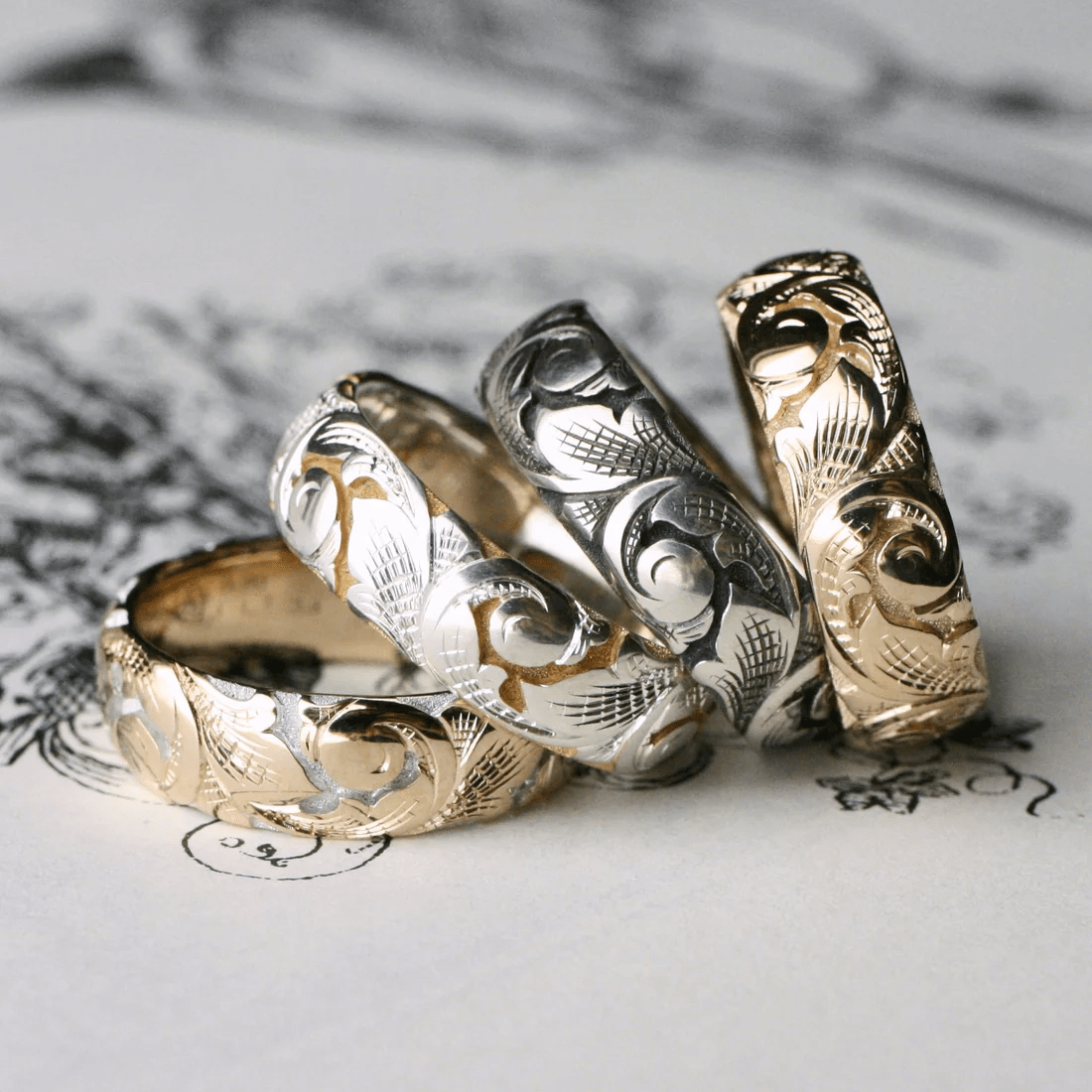 Set of slim acanthus engraved bands in mixed metals arranged on decorative background.
