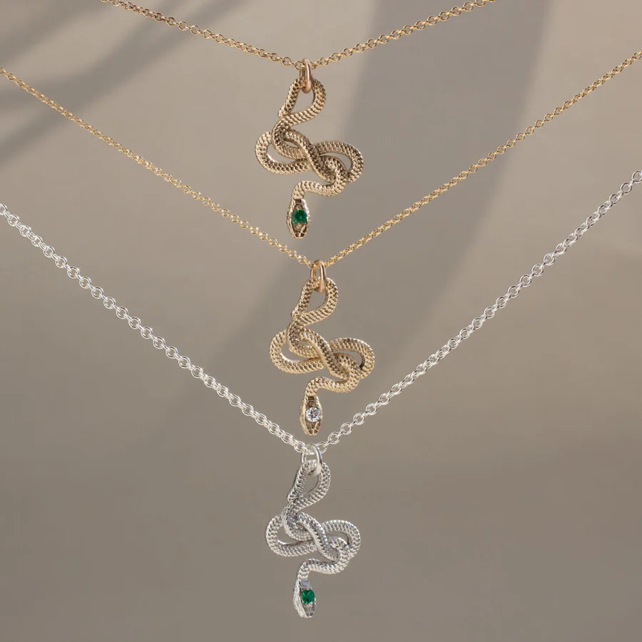 Snake Guardian Necklaces hanging from  delicate sterling silver chains, showing the sculptural snake pendants and green emerald details
