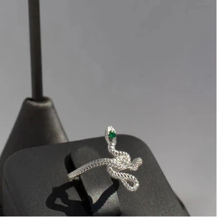 Snake Guardian Ring displayed on a jewelry stand, highlighting its sculptural sterling silver snake design and emerald gemstone.