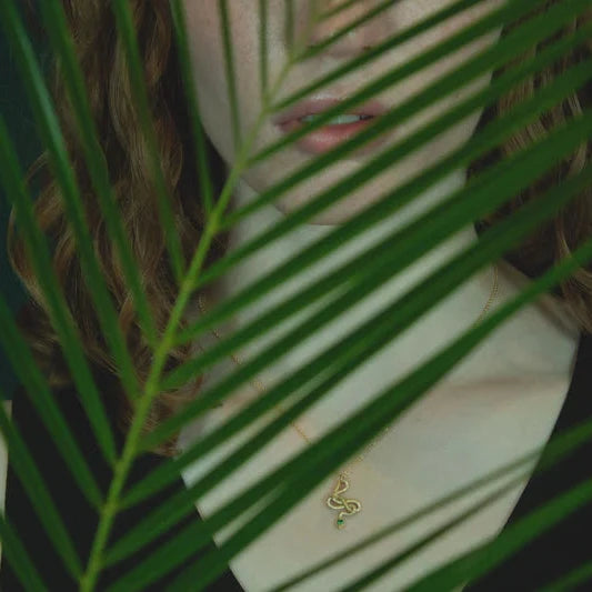 Sterling silver Snake Guardian Necklace shown behind a tropical green leaf background, highlighting its serpent-inspired design and emerald accent.