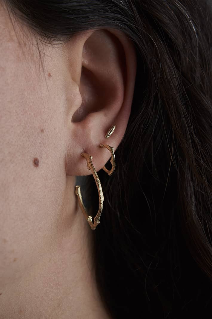 Close-up of a model wearing Sprig Hug Hoop Earrings in yellow gold, showcasing their petite size and organic branch-inspired texture.