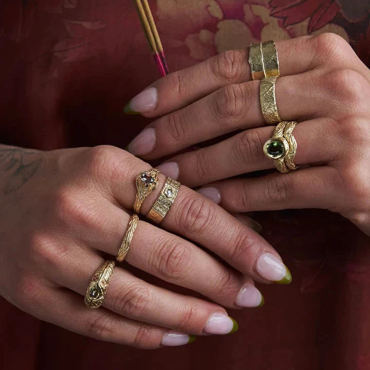 Close-up of hands wearing a collection of sculptural gold rings, including the 14k yellow gold Sprig Ring with its delicate wood-grain texture and stackable design.