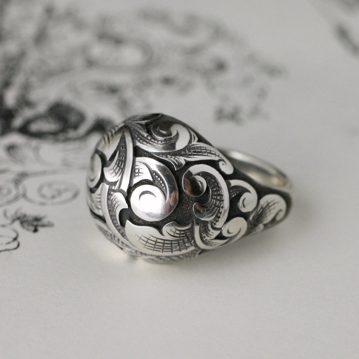 Front view of the sterling silver Bombe Ring, highlighting its raised scroll patterns, darkened recessed details, and polished silver finish.