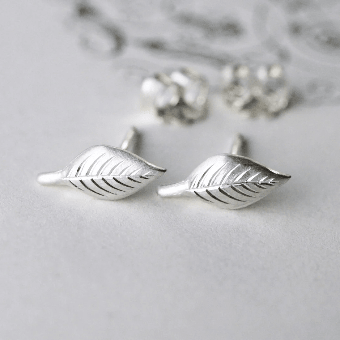Sterling silver hand-engraved leaf stud earrings displayed on a light background.