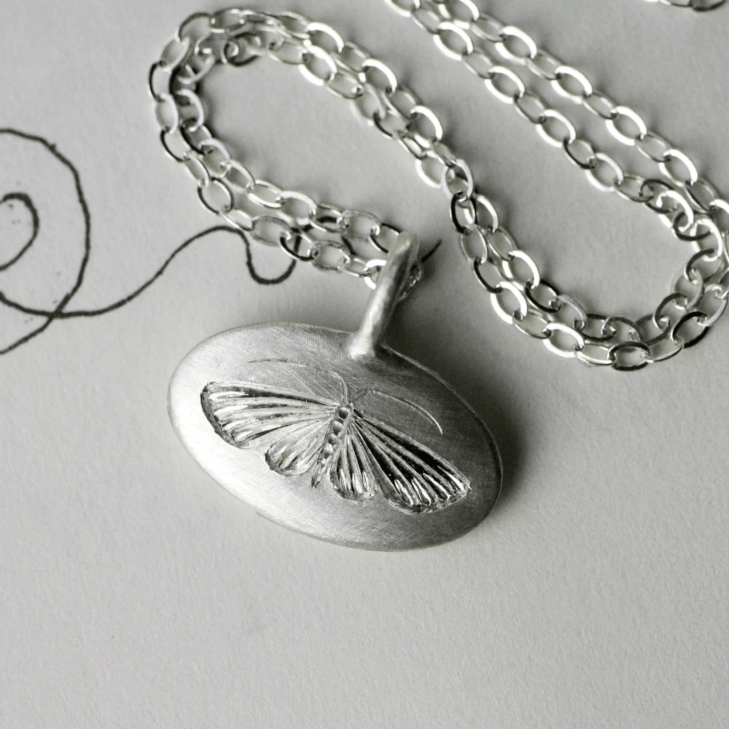 Sterling silver hand-engraved house moth pendant displayed on a chain.