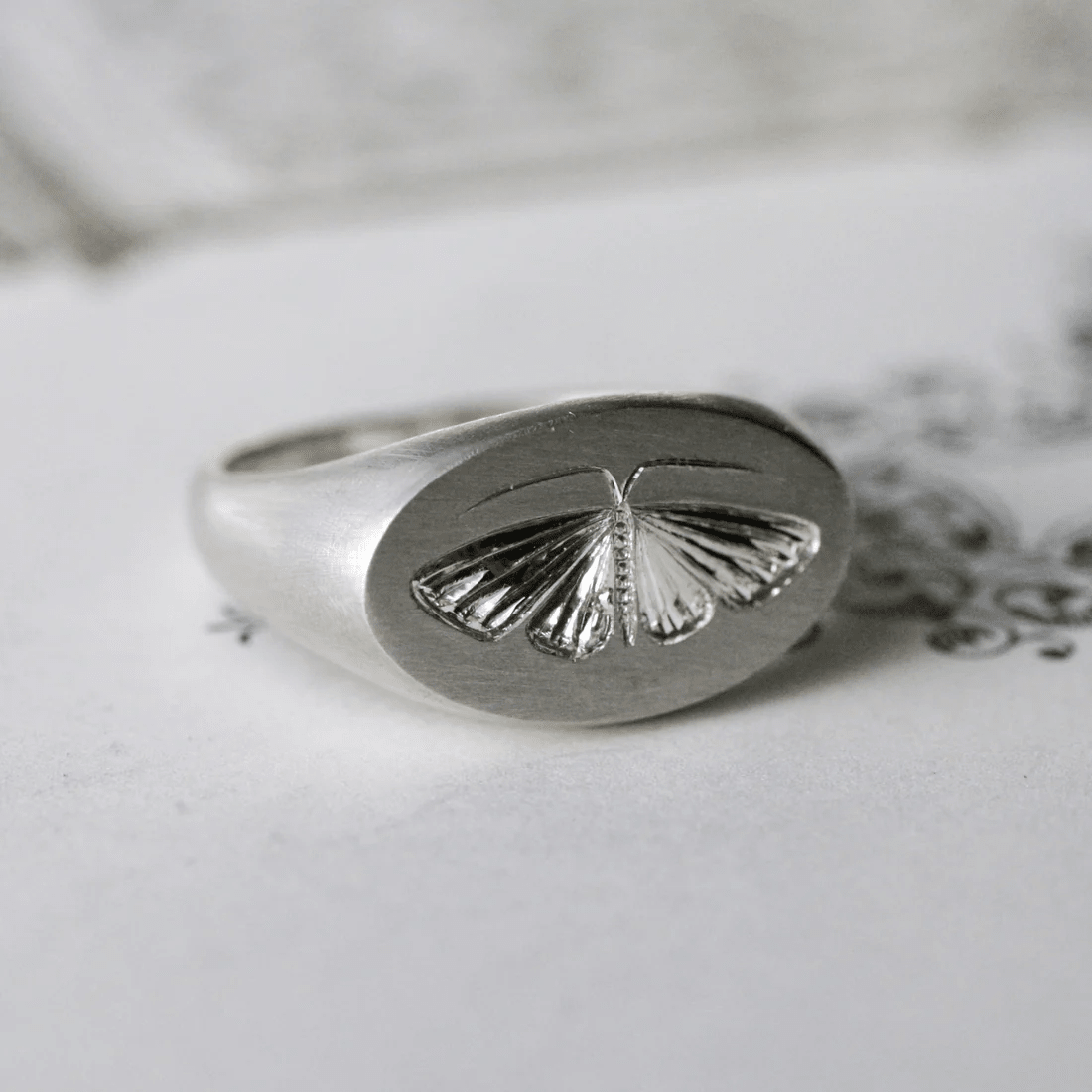 Close-up of a sterling silver house moth ring displaying the hand-engraved moth design.
