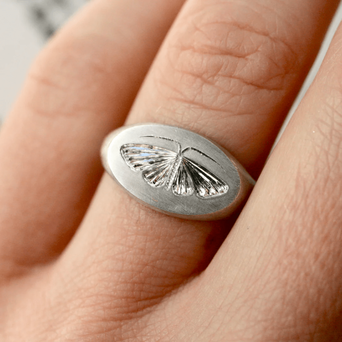 Sterling silver house moth ring worn on a finger, showing the engraved moth design.