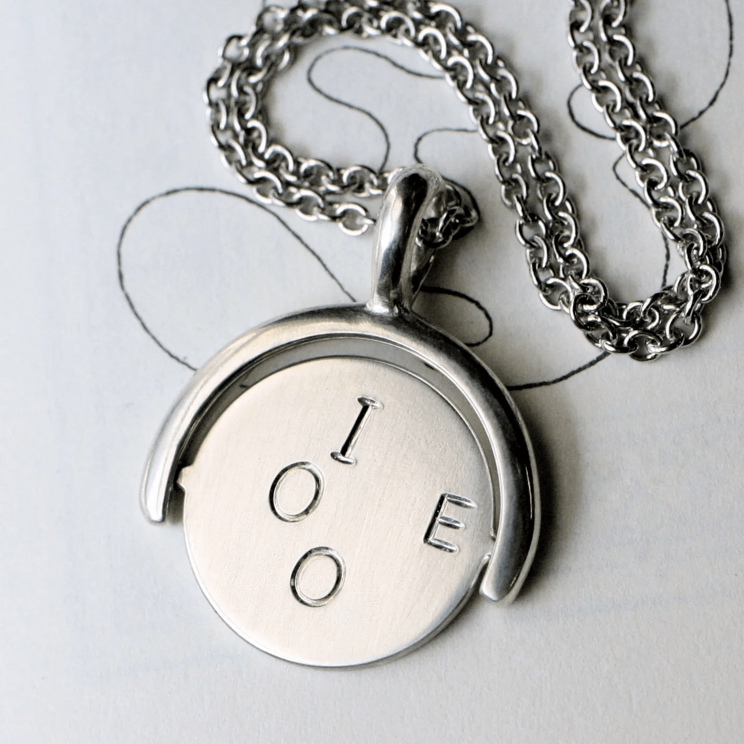 Close-up of sterling silver spinner pendant showing engraved I O E side.