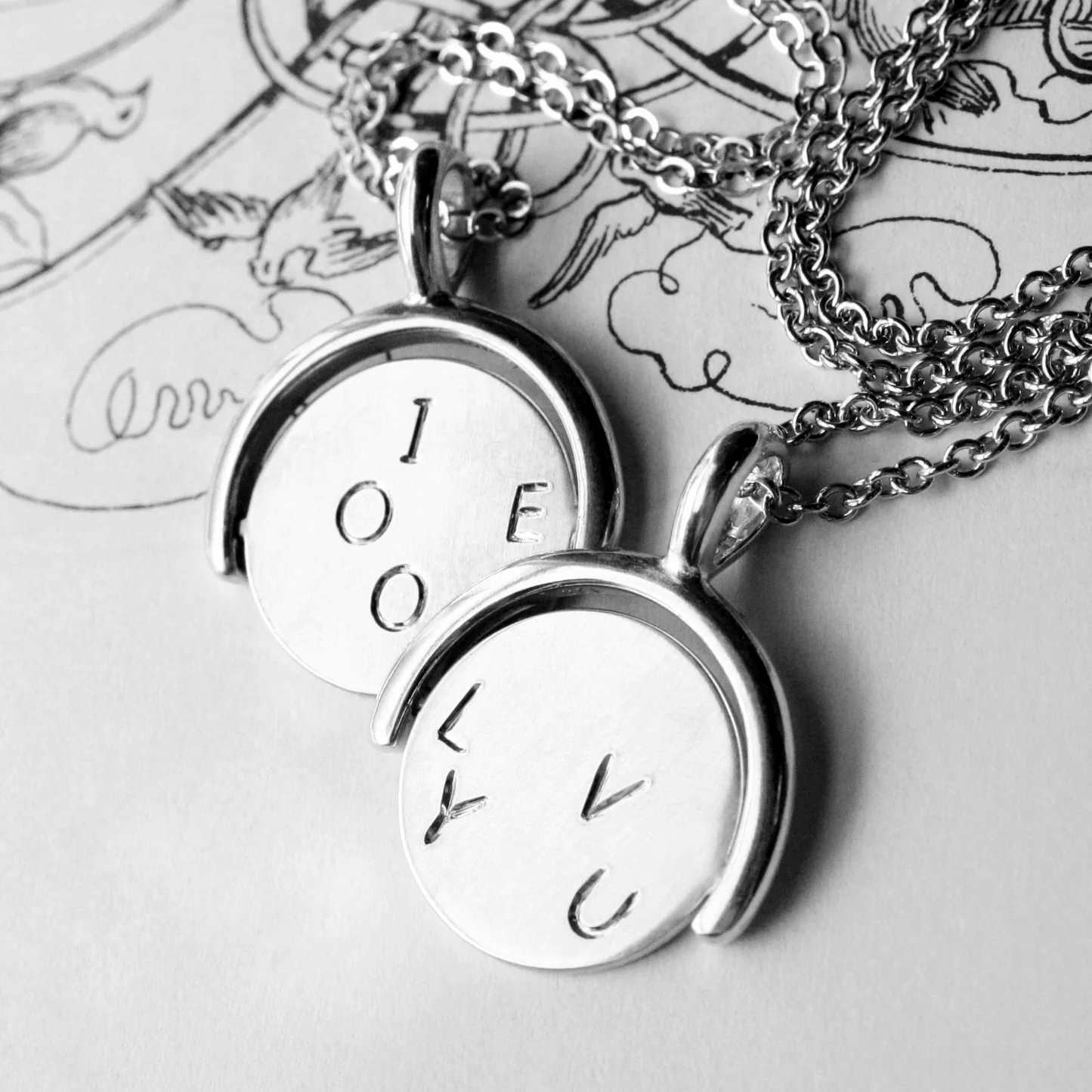 Sterling silver spinner pendant with hand-engraved letters displayed on a chain.