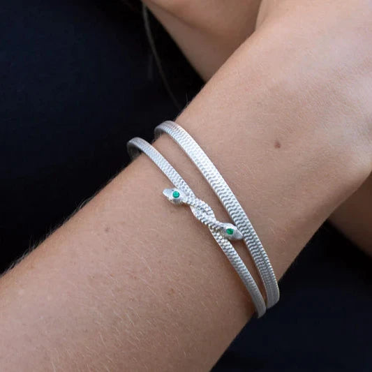 Model wearing the Symbiosis sterling silver snake cuff bracelet with two green emerald accents, showing its elegant fit on the wrist.