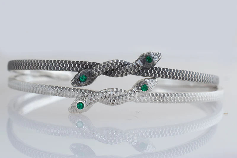 Detailed view of the Symbiosis sterling silver cuff bracelet highlighting the sculptural snake heads, green emerald gemstones, and handcrafted silver finish.