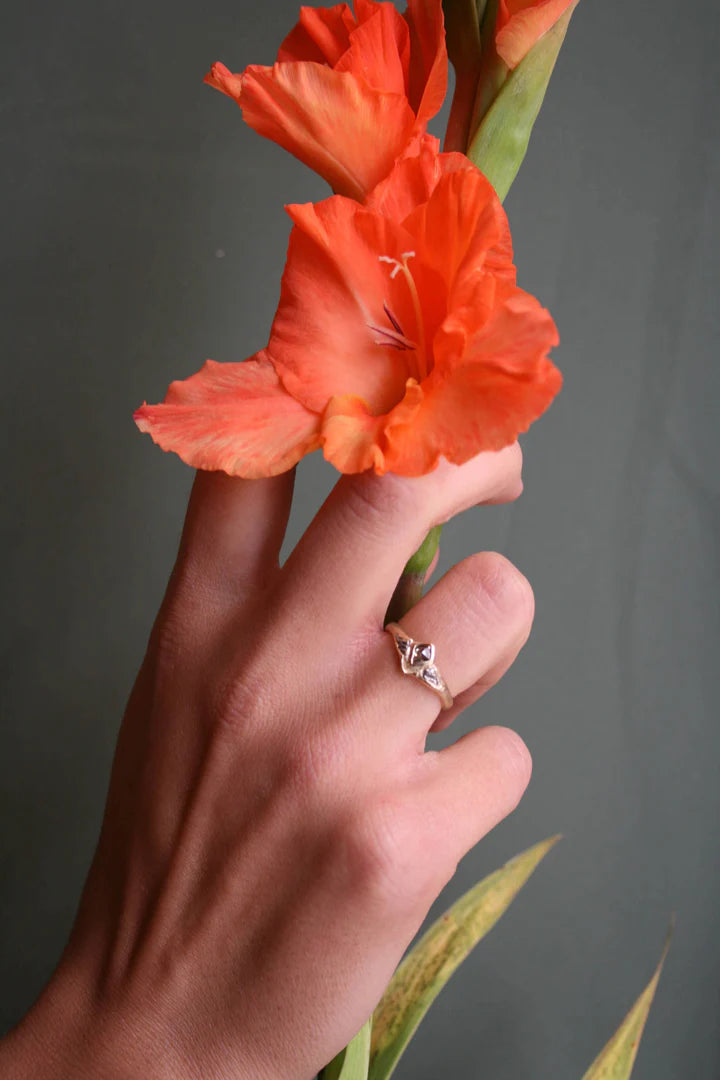 Tava Kite Diamond Ring worn on a hand holding an orange flower, showcasing its organic 14k gold setting and nature-inspired design.