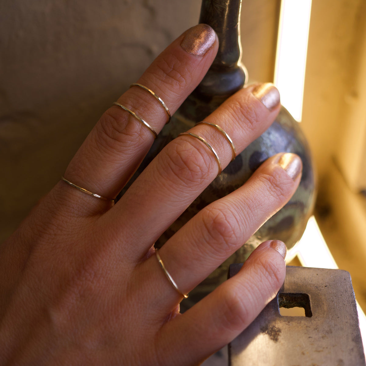 Teko Gallery's thin 14k solid gold hammered stacking ring worn with other gold bands on a hand, showing its delicate proportions and textured finish.