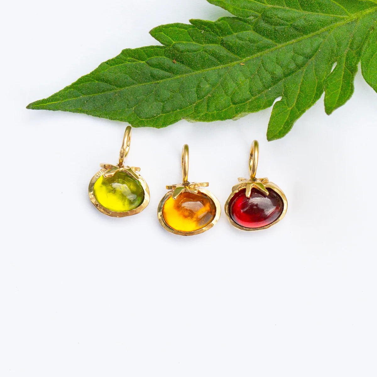 Group of 14k yellow gold tomato charms with stones on leaf background