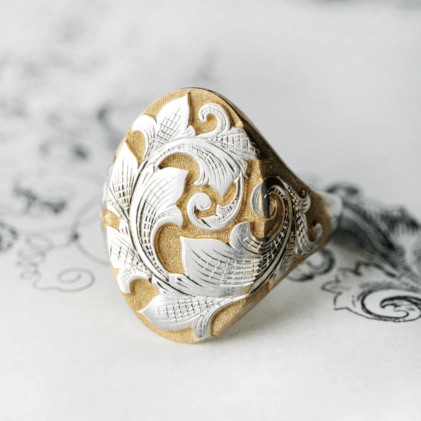 Two-tone acanthus engraved signet ring on white background – north-south scroll ring