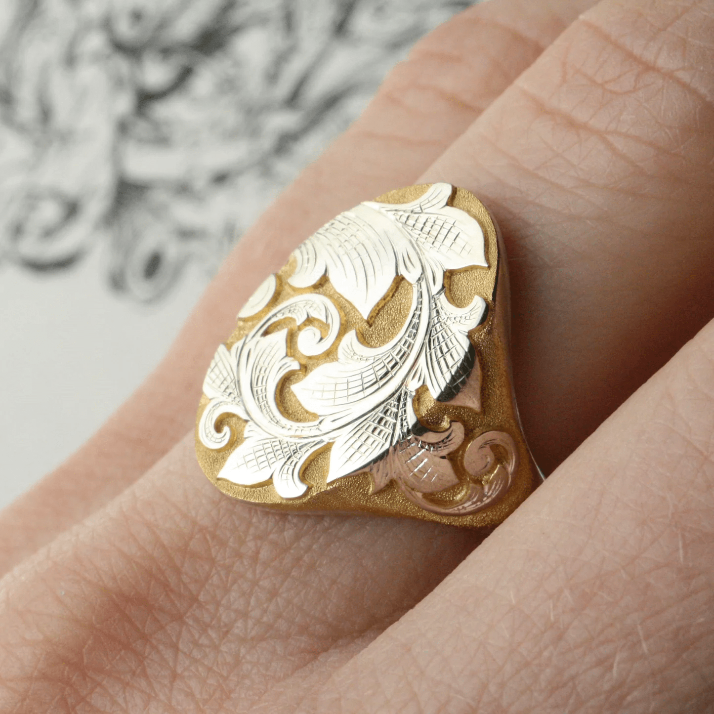 Two-tone acanthus signet ring worn on finger – engraved north-south scroll design