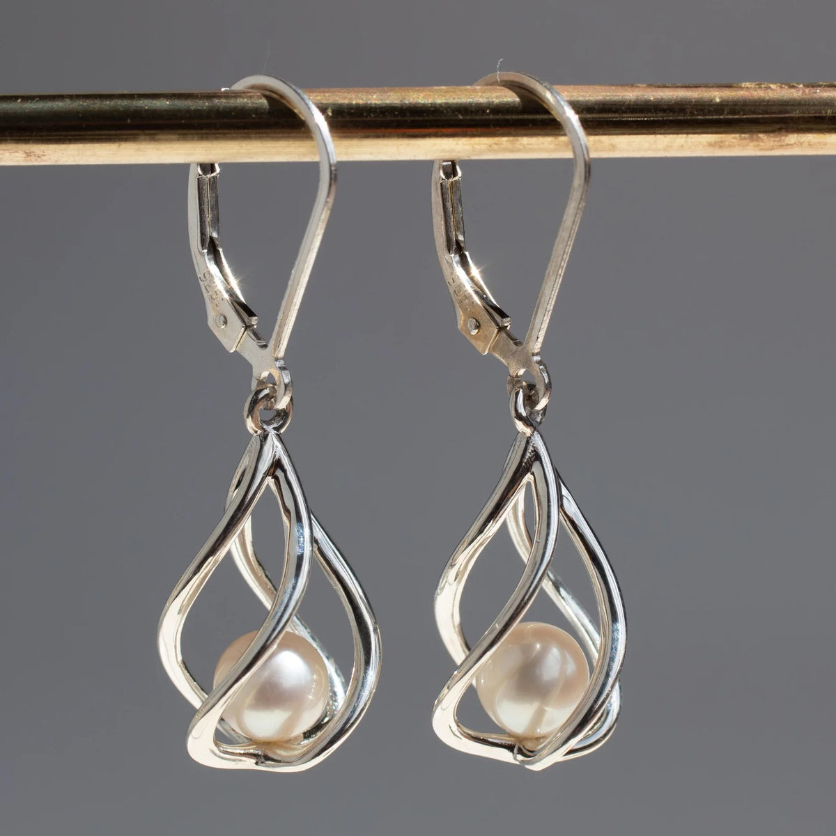 Pair of Vine Earrings hanging on a display, highlighting their twisting sterling silver forms and freshwater pearl drops.