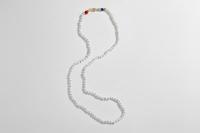 Long necklace made of small white beads with colored accents, arranged in a loose curve against a pale background.