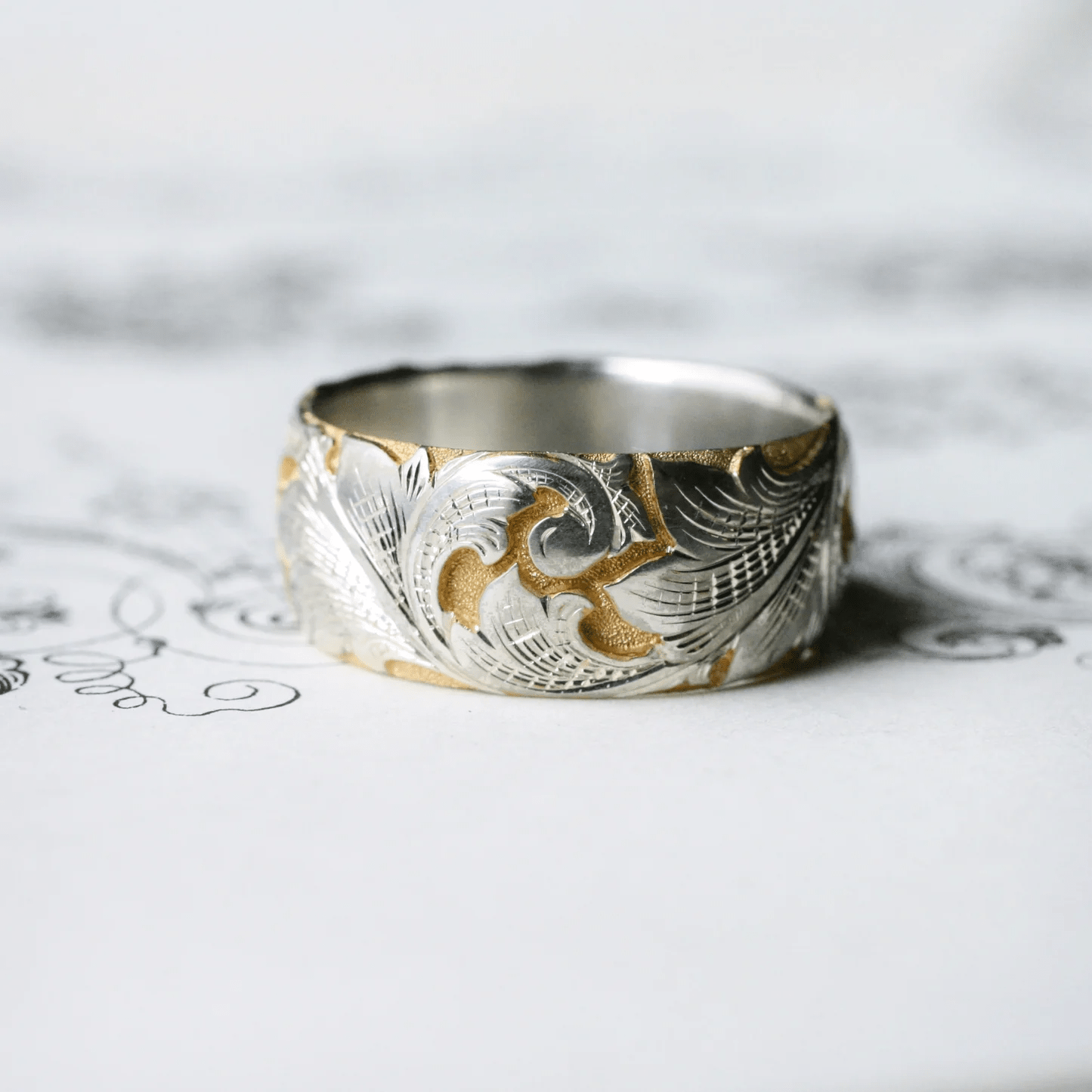 Wide two-tone acanthus ring on decorative background – engraved scroll and leaf design.