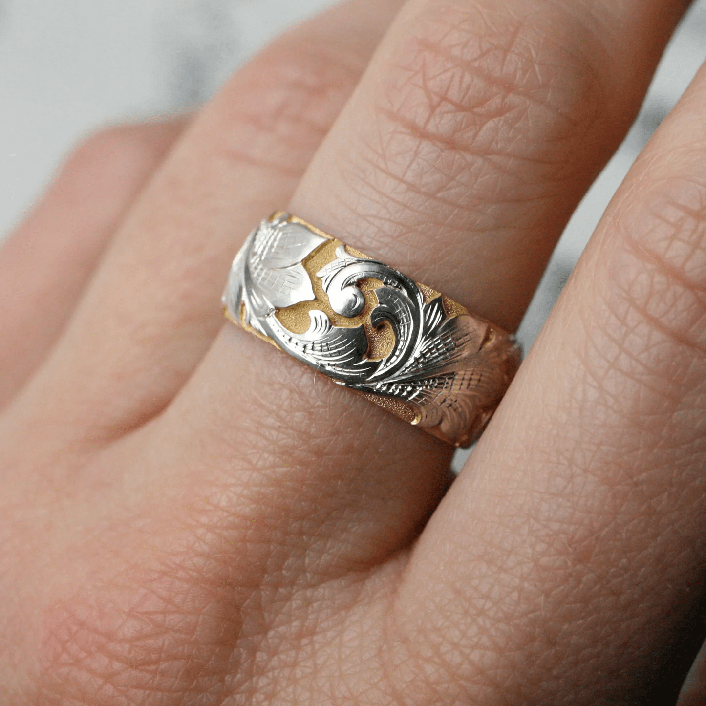 Wide two-tone acanthus engraved ring worn on hand – sculptural scroll and leaf pattern.